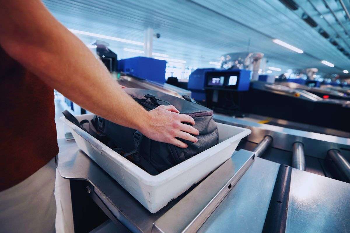 uomo in aeroporto che mette valigia sul rullo del metaldetector