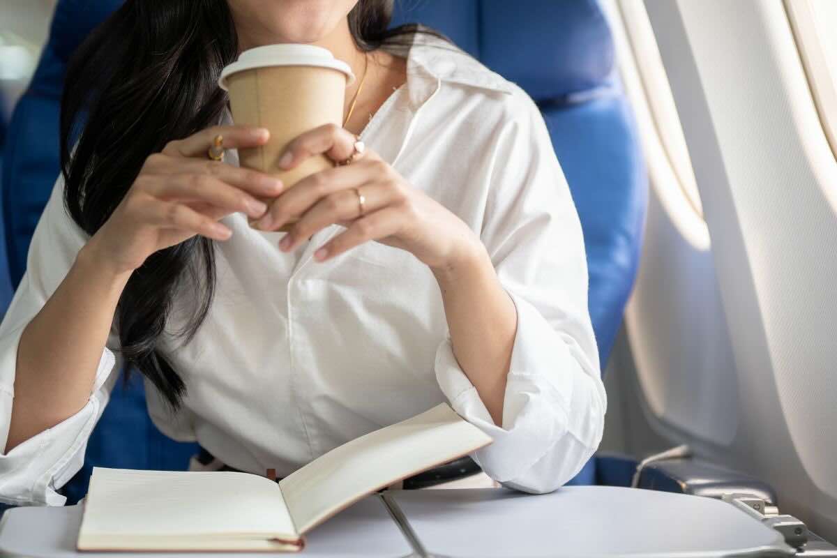 Mani di donna con contenitore bevanda in mano sull'aereo
