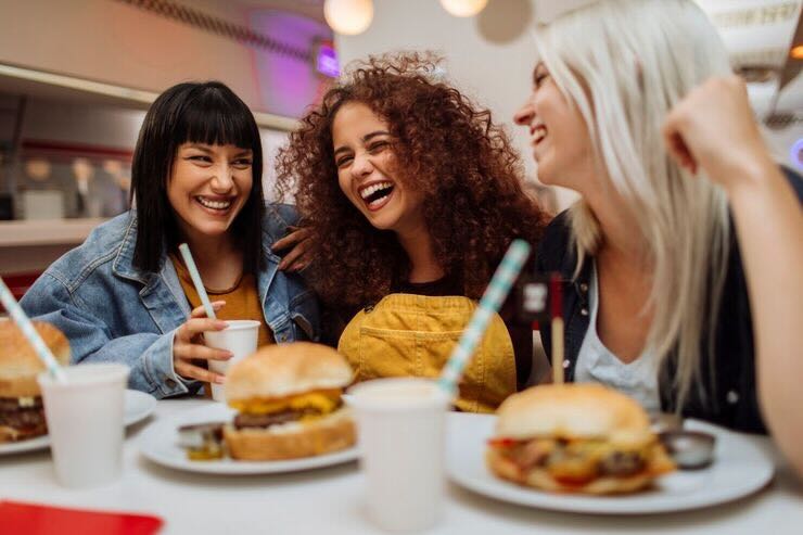 Ragazze mangiano con hamburger sul tavolo, sorridenti