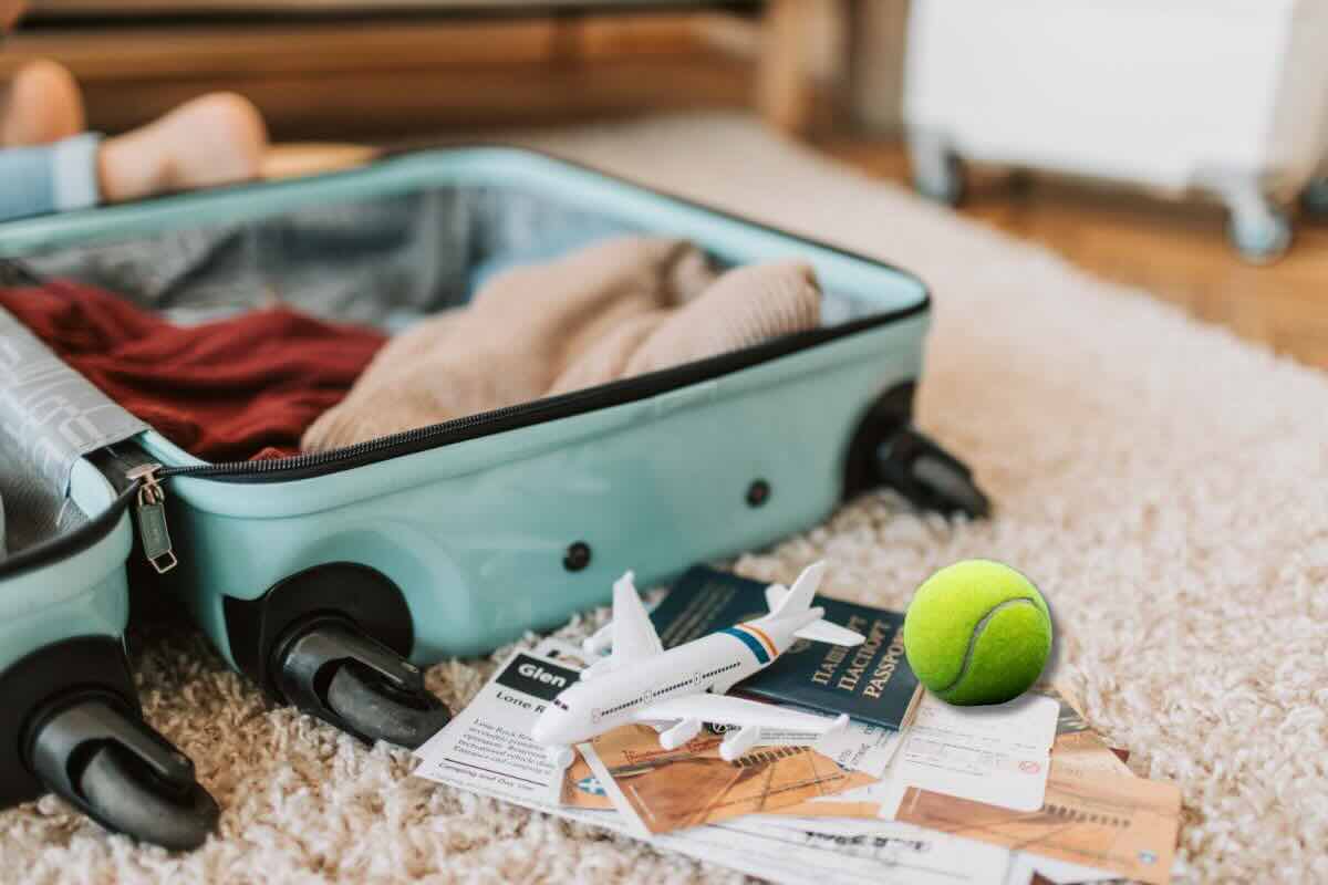 Valigia poco piena, documenti sul tappeto, pallina da tennis