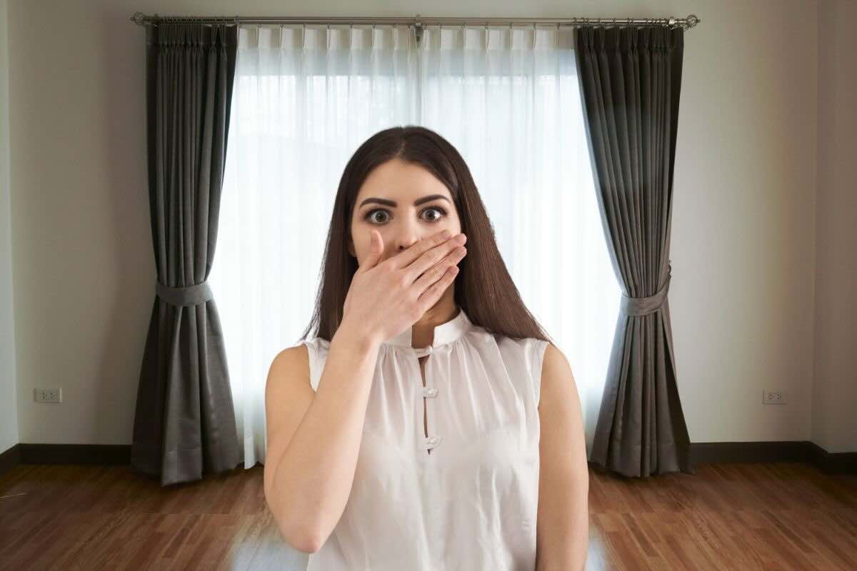 Donna con mano sulla bocca, tende dietro di lei
