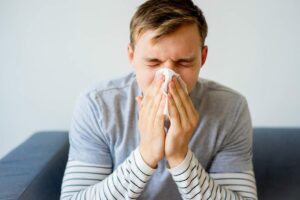 uomo seduto sul divano che si soffia il naso con fazzoletto