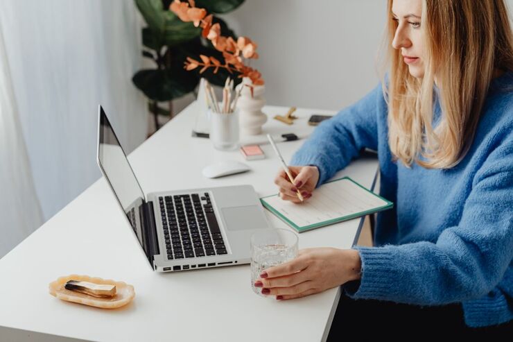 Donna che scrive qualcosa su un quaderno alla scrivania guardando il PC