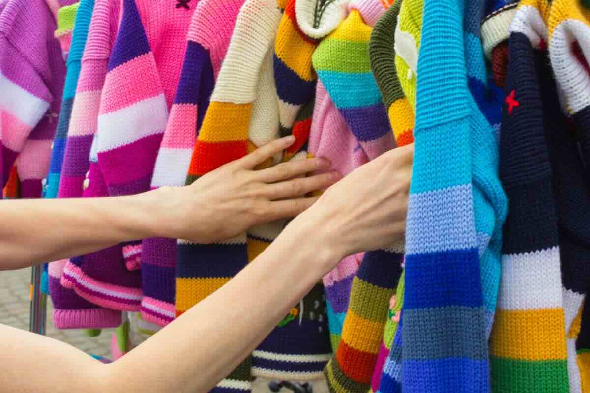 Rovistare con le mani fra maglie appese tutte colorate