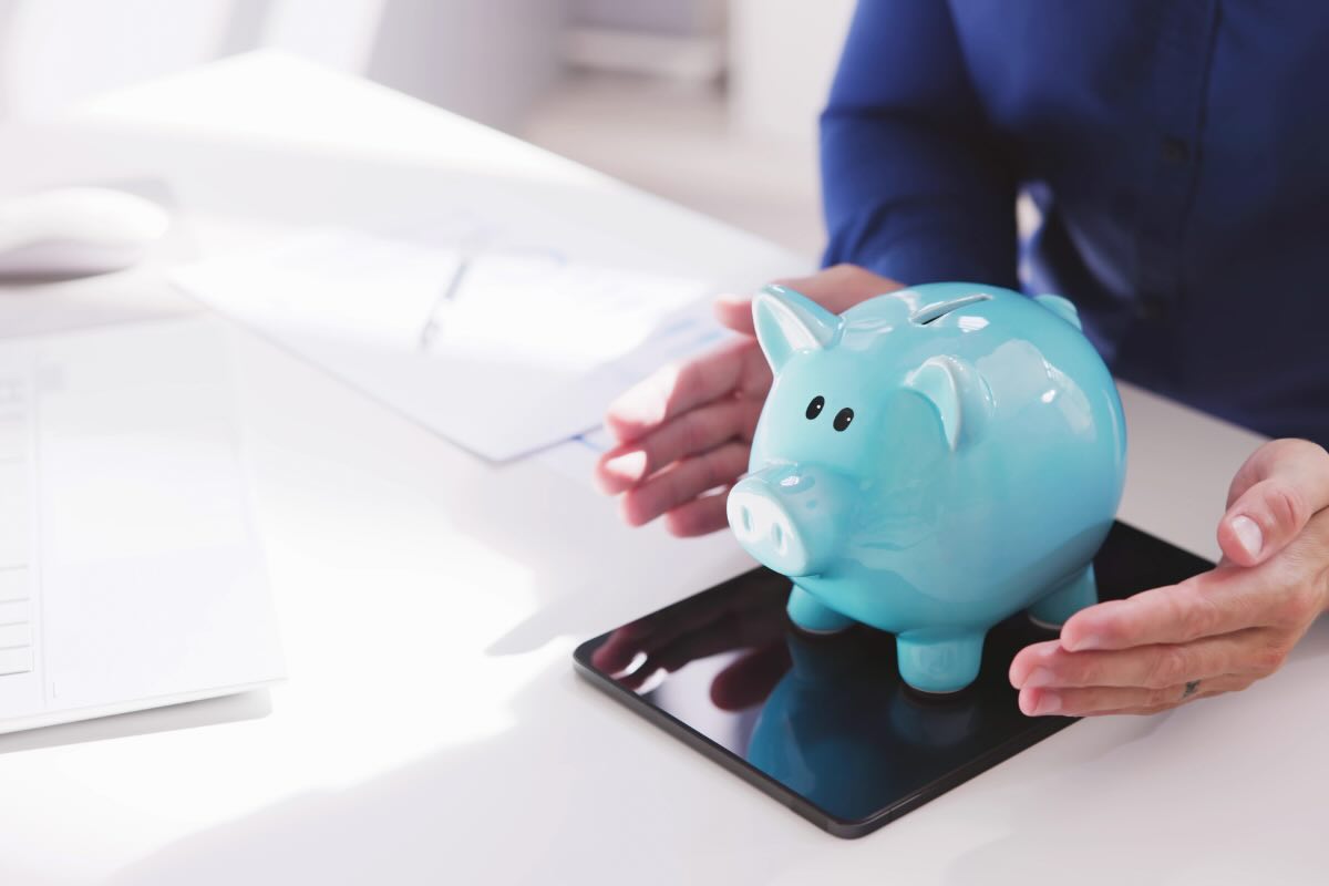 mani che tengono salvadanaio azzurro e tablet