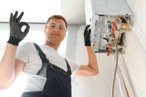 uomo con occhiali trasparenti che fa ok con la mano e con l'altra si appoggia ad una caldaia