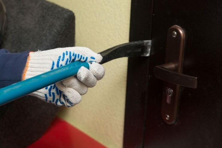 Ladro con guanti bianchi e azzurri usa un oggetto di ferro per aprire la porta