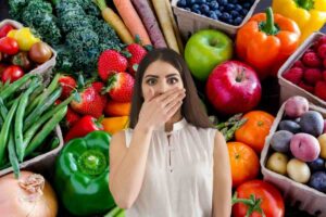 Donna con mano sulla bocca, frutta e verdura dietro di lei